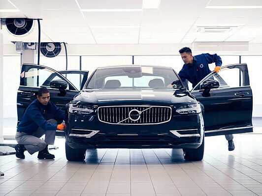 Schwarzer Volvo in der Werkstatt wird von zwei Mitarbeitern gereinigt